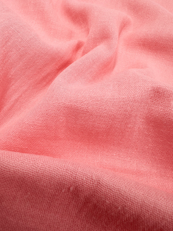 A detailed view of the Muslin - Flamingo Pink - 145cm by Super Cheap Fabrics reveals its soft, wrinkled texture with a linen weave. The organic fabric showcases gentle folds and shadows, highlighting its supple quality and vivid color.