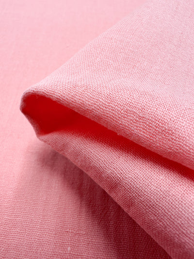 Close-up of a folded piece of Muslin - Flamingo Pink - 145cm by Super Cheap Fabrics, highlighting its texture and weave. The organic fabric looks soft and lightweight, with a subtle sheen.