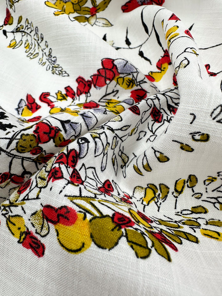 Close-up of Super Cheap Fabrics' Linen Blend - Scarlet Vine, featuring vibrant floral patterns in red, yellow, and green. The crumpled fabric showcases intricate flower and leaf designs—ideal for summer outfits. Width: 145cm.