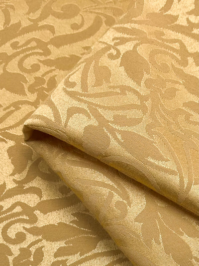 A close-up of the Designer Damask - Oak Buff fabric by Super Cheap Fabrics displays a luxurious jacquard texture with an ornate, swirling floral pattern, enhancing its elegant appearance.