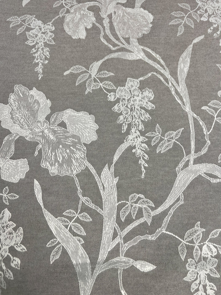 The Designer Damask - Saphire Dust by Super Cheap Fabrics showcases an ornate and delicate design, where white thread intricately embroiders a variety of botanical elements including intertwined leaves and flowers, all set against a luxurious gray fabric background.