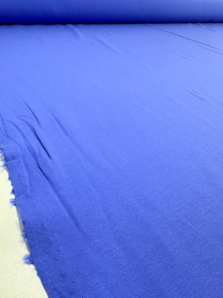 The Nebulas Blue Cotton Lycra from Super Cheap Fabrics, measuring 165cm, displays a smooth surface with subtle creases and slight fraying at the edges, ideal for adding charm to tailoring or crafting projects.