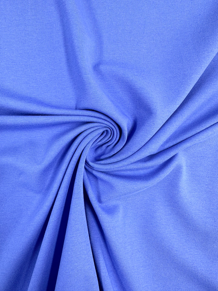 A close-up of Super Cheap Fabrics’ Cotton Lycra in Nebulas Blue, 165cm wide, twisted into a spiral at the center. This medium-weight material has a soft and flowing texture, creating dynamic folds and shadows.