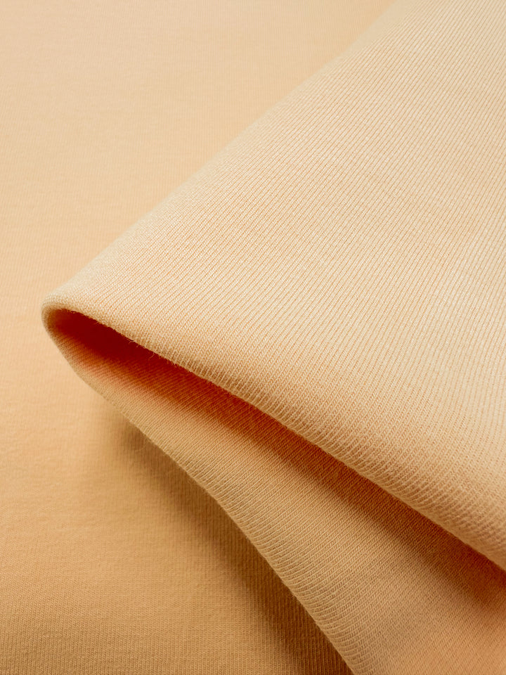 A close-up of Super Cheap Fabrics' Cotton Lycra in Caramel Cream (165cm) reveals a soft, light peach texture with smooth fibers and a subtle shine, offering extra comfort.