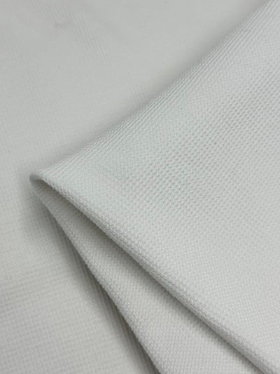 Close-up of folded **Honeycomb Knit - White - 158cm** fabric by **Super Cheap Fabrics** with a fine 3D texture. The fabric appears smooth and slightly reflective under the light, and the folds create a soft play of shadows.