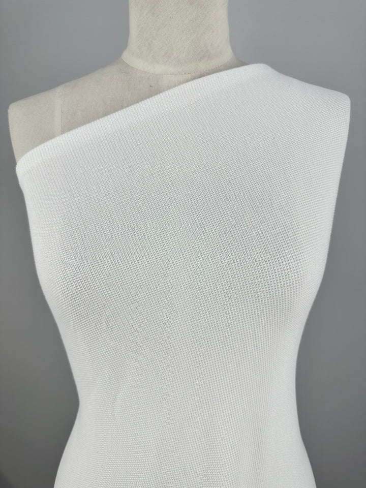 A white mannequin dressed in a form-fitting, one-shoulder white dress made of Honeycomb Knit - White - 158cm by Super Cheap Fabrics is displayed against a plain gray background.