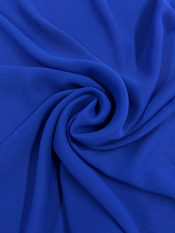 Close-up of vibrant Hi-Multi Chiffon in royal blue, showcasing its lightweight fabric artfully gathered into a swirl pattern. The texture appears smooth, with light reflecting off the delicate folds, creating subtle variations in the shade of blue, reminiscent of floaty tops that elegantly catch the breeze. This exquisite fabric is brought to you by Super Cheap Fabrics and spans a width of 150cm.