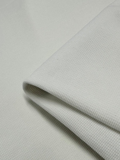 A close-up view of a folded piece of Honeycomb Knit - Vanilla - 158cm by Super Cheap Fabrics. The material has a slightly rough surface with a subtle woven pattern reminiscent of honeycomb fabric, and the edges are neatly aligned. The lighting highlights the texture, creating a three-dimensional effect and adding depth and dimension.
