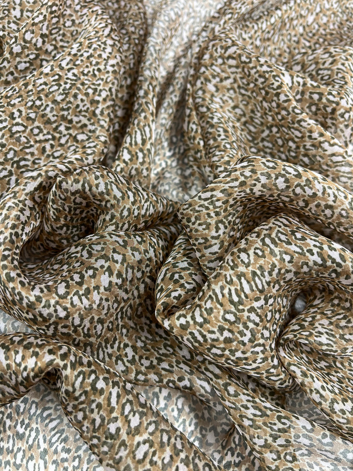 Close-up of light, flowy Pure Printed Silk - Namir fabric from Super Cheap Fabrics featuring a small leopard print pattern. The multi-colour fabric showcases shades of brown, beige, and cream, elegantly draped in folds to emphasize its delicate and airy 75 GSM texture. The fabric width is 135 cm.