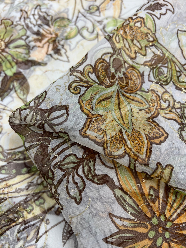 A close-up shot of Pure Printed Silk - Jaipur - 130cm by Super Cheap Fabrics, showcasing intricately patterned fabric with a floral motif in shades of green, brown, and beige. The lightweight material appears airy, with subtle shimmers of gold thread woven throughout the multi-colored design.