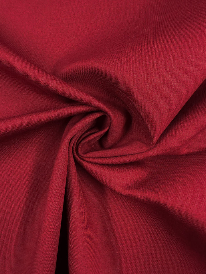 A close-up of Super Cheap Fabrics' Milano Ponte - Cabernet - 160cm highlights the smooth, deep red fabric with a soft texture, showcasing gentle folds and a central swirl pattern.