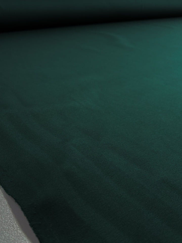 A close-up of Super Cheap Fabrics' Milano Ponte - Pine Grove (160cm), a dark green heavyweight ponte fabric, neatly displayed to highlight its subtle texture and soft folds—ideal for structured skirts.