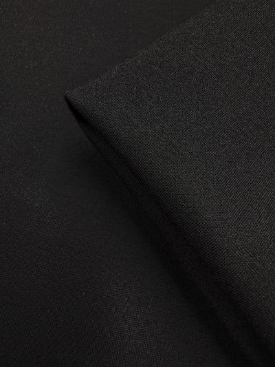 Close-up of Milano Ponte - Black - 160cm by Super Cheap Fabrics, highlighting its smooth texture and subtle weave. A folded corner creates a sharp edge, showcasing this versatile heavyweight fabric's quality.