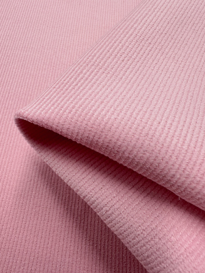 Close-up of soft Micro Wale Corduroy from Super Cheap Fabrics in Tickled Pink, ideal for winter wear, highlighting its ribbed texture and folded layers. Width 142cm.