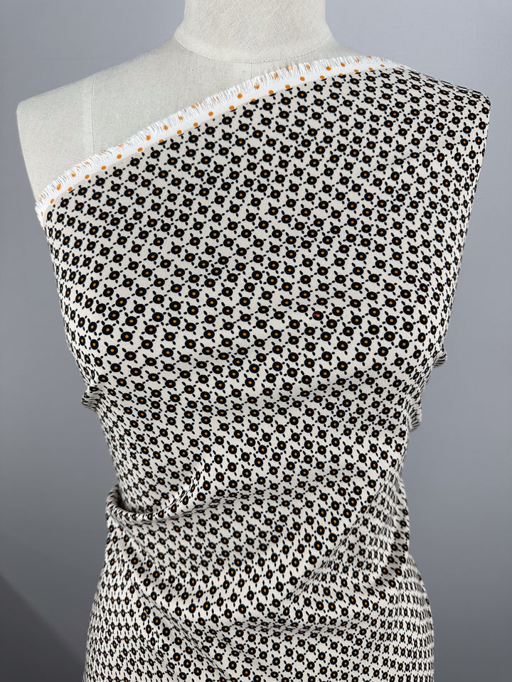 A mannequin displays the "Printed Bengaline - Radar - 150cm" by Super Cheap Fabrics, featuring a medium-weight black and white geometric pattern with small circular designs. The two-way stretch woven material is draped asymmetrically over one shoulder against a plain background.