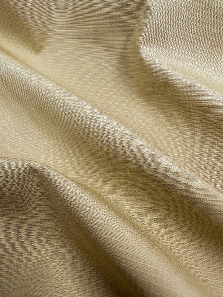 Close-up of the Textured Grid Cotton in Curry, a 150cm wide fabric by Super Cheap Fabrics. The beige color and grid pattern drape softly, highlighting its unique surface texture with gentle folds and shadows.