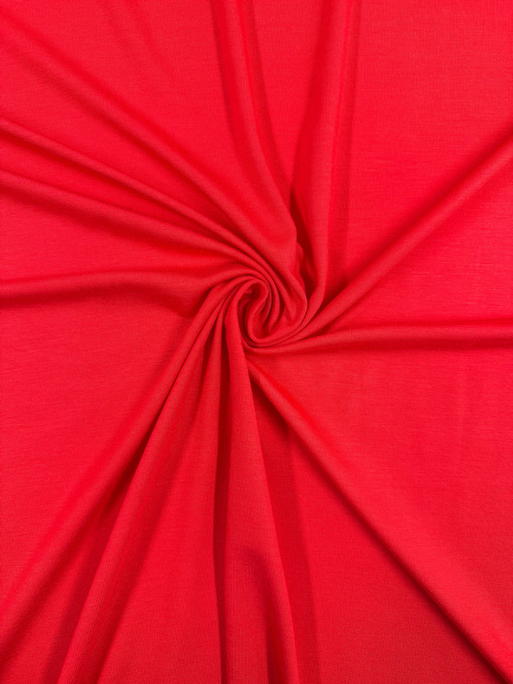 Super Cheap Fabrics' Cotton Lycra - Hibiscus - 165cm features a vibrant red hue in a spiral twist pattern, with soft, dynamic folds. This medium-weight, stretchy fabric offers excellent flexibility for various projects.