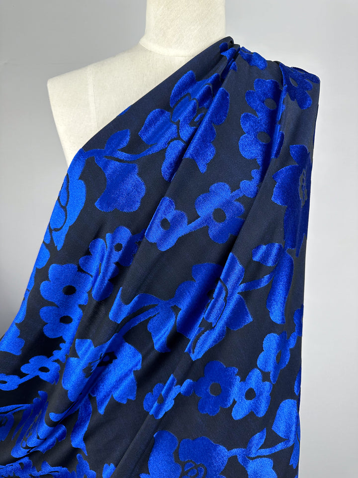 A mannequin is adorned with Super Cheap Fabrics' 155cm Burnout Velvet in Snorkel Blue, displaying a vivid blue and black floral pattern. The design features bold, abstract electric blue flowers on a black backdrop for a striking contrast.