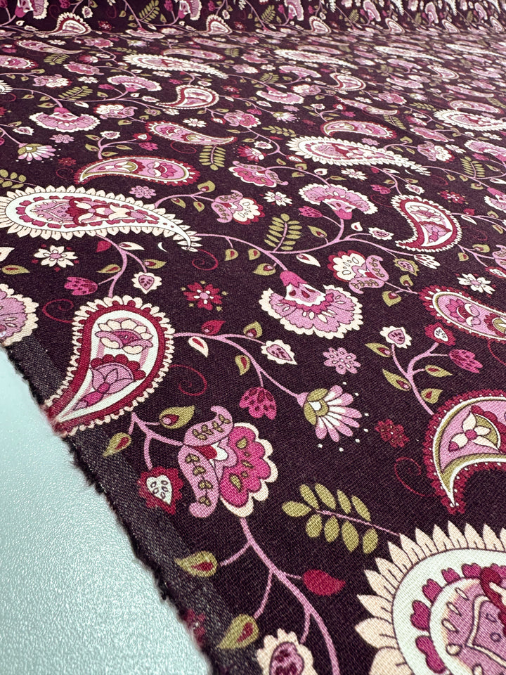 Close-up of Linen Blend - Paisley - 140cm by Super Cheap Fabrics, featuring a colorful paisley pattern with pink, purple, and green floral designs on a dark background. The medium-weight linen fabric is spread out to showcase intricate details and vibrant colors ideal for home decor.