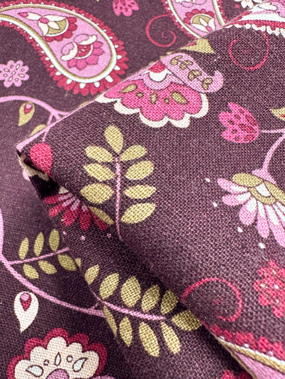 The Super Cheap Fabrics Linen Blend - Paisley, 140cm, showcases a rich patterned fabric with pink, lime green, olive, and off-white paisley and floral designs on a deep purple background. It's medium weight and ideal for home decor.