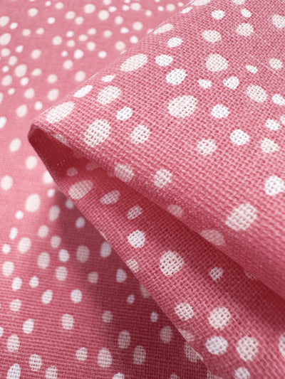 A close-up of Super Cheap Fabrics' Linen Blend - Spotty 140cm fabric shows its textured weave with pink and white polka dots. The folded material creates a gentle shadow and highlights the contrast, making it ideal for home decor accents.