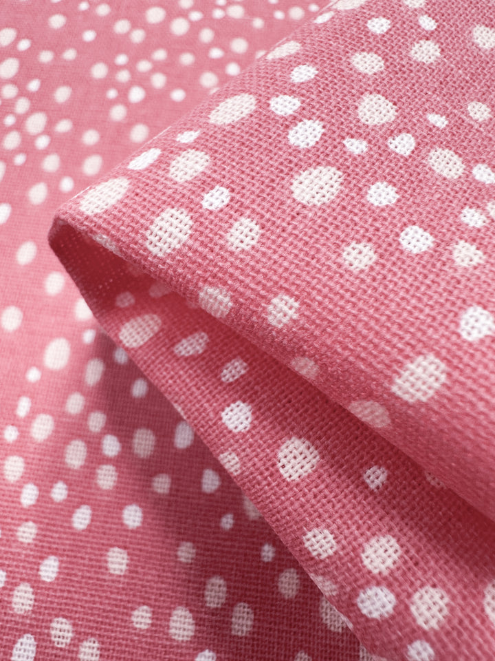 A close-up of Super Cheap Fabrics' Linen Blend - Spotty 140cm fabric shows its textured weave with pink and white polka dots. The folded material creates a gentle shadow and highlights the contrast, making it ideal for home decor accents.