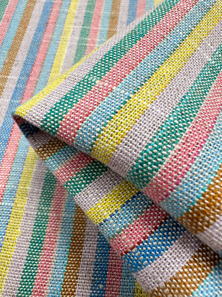 The Linen Blend - Tropicana by Super Cheap Fabrics is a 143cm wide, folded, woven fabric with vintage-style yarn-dyed stripes in pink, blue, yellow, brown, and green on a light background for a vibrant and textured appearance.