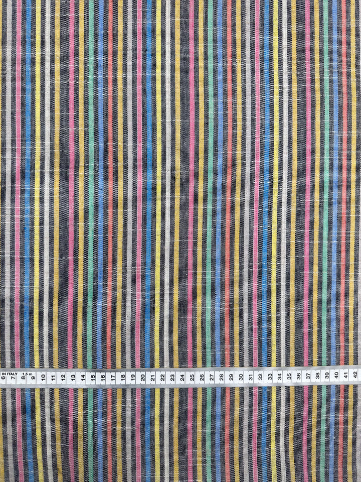 The "Linen Blend - Beachside - 143cm" by Super Cheap Fabrics showcases a vintage look with vertical stripes in vibrant colors such as yellow, blue, green, red, and black. A measuring tape at the bottom shows it's medium weight and extends to 50 cm.