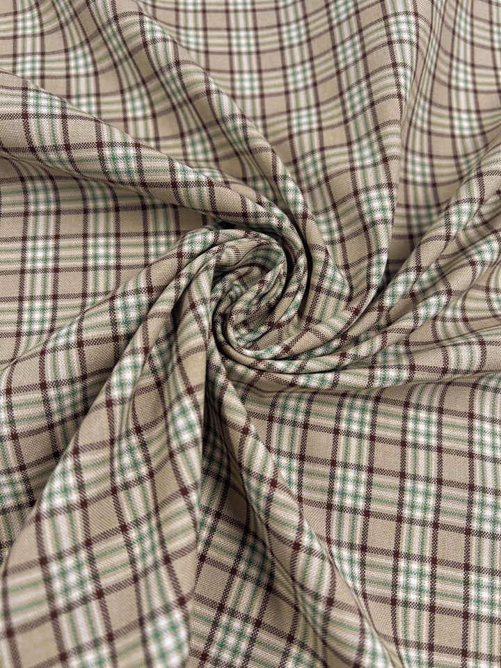 Close-up of the Shirting - Safari fabric by Super Cheap Fabrics, showcasing a plaid pattern with beige, brown, and green lines. This light to medium weight polyester cotton material is gathered and twisted at the center, forming a textured spiral design.