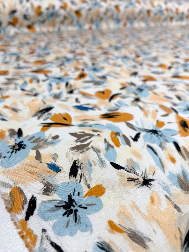 A close-up of Super Cheap Fabrics’ Mercerised Rayon - Autumn Haze (150cm), showcasing lightweight, breathable rayon with a blue, yellow, black, and beige floral brushstroke design on a white background laid flat.