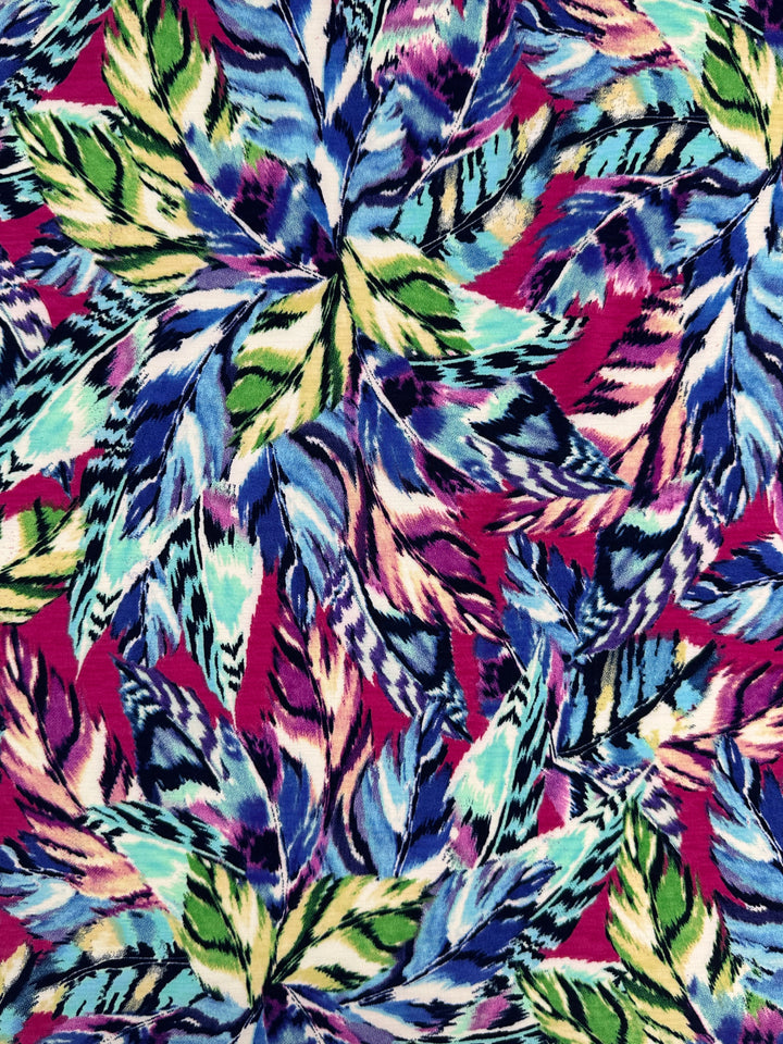 The medium-weight Printed Lycra - Wavy by Super Cheap Fabrics features a vibrant pattern of abstract leaves in blue, green, yellow, and pink on a magenta background. Made from a polyester/spandex blend, it combines sharp and soft edges for an energetic aesthetic. Width: 150cm.