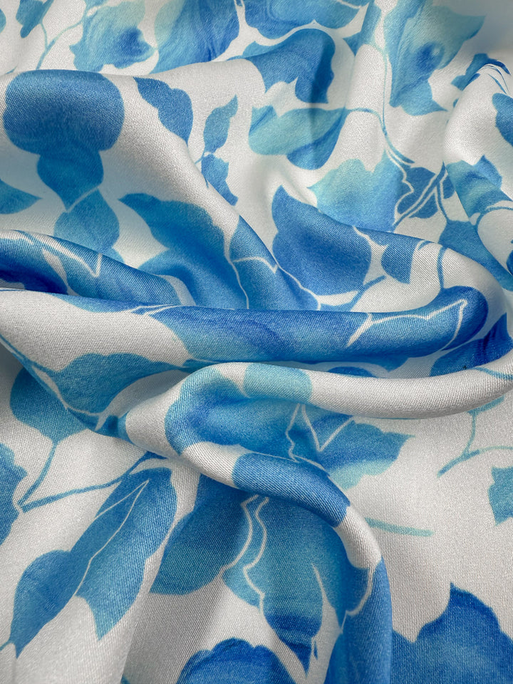 A close-up of Super Cheap Fabrics' Mercerised Rayon - Blue Ginkgo (150cm), featuring smooth, lightweight fabric with a blue ginkgo leaf pattern, showing folds and soft shadows that highlight its texture and vibrant watercolor style.
