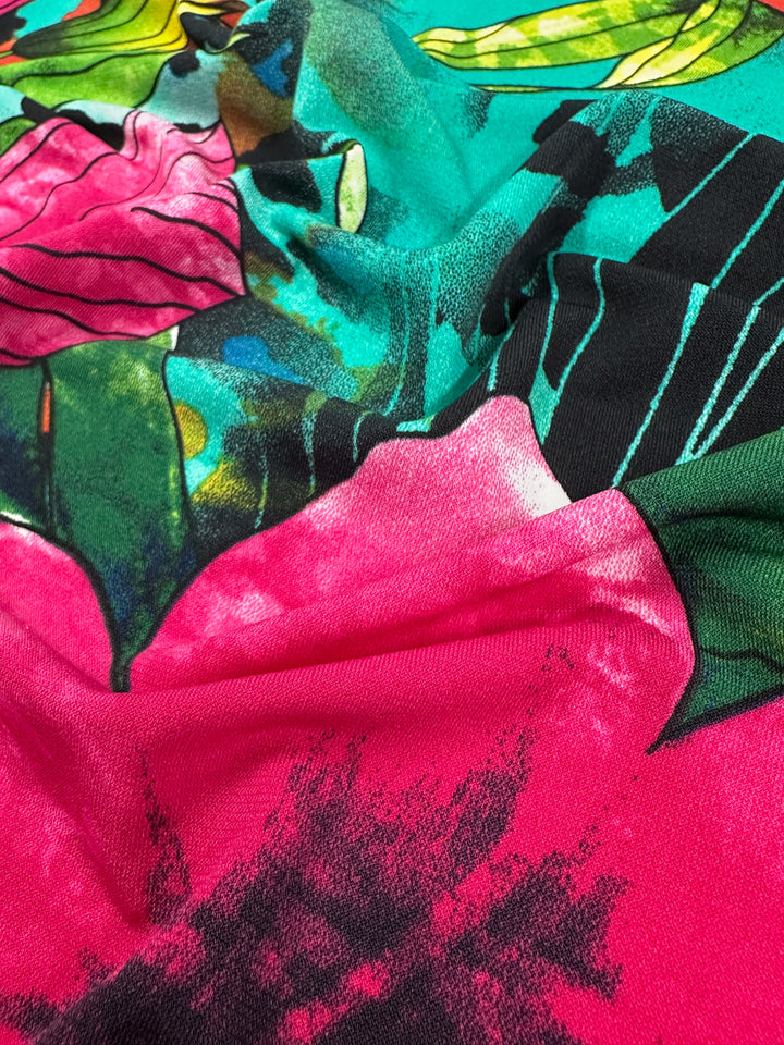 The Super Cheap Fabrics Printed Lycra - Aqua Flora - 150cm features a vibrant tropical design with bold pink petals, green leaves, and dark black accents. Its medium weight and dynamic colors create a lively appearance.