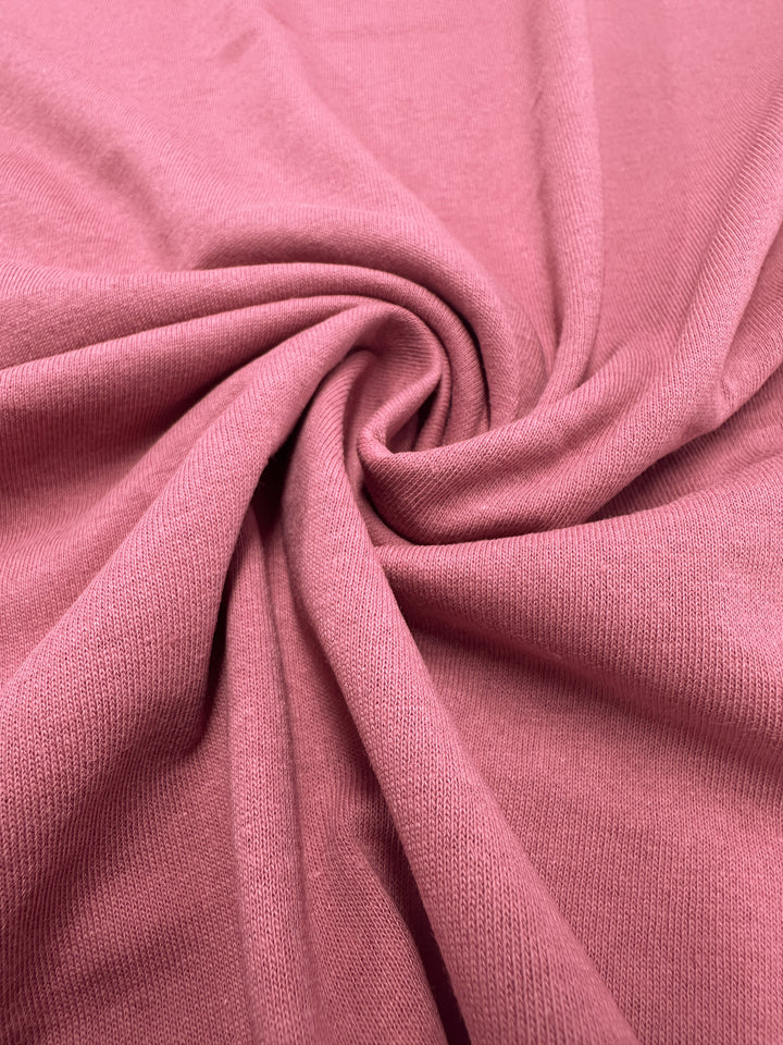 Close-up of Super Cheap Fabrics Cotton Jersey in Slate Rose, 175cm width, featuring a pink fabric with a smooth, softly ribbed texture and gathered into a spiral pattern that creates gentle folds and shadows.