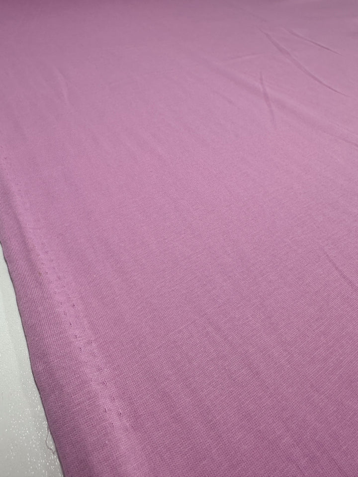 The Cotton Jersey - Pastel Lavender by Super Cheap Fabrics, measuring 160cm, displays its smooth texture on a flat surface with subtle creases. The fabric diagonally spreads from the bottom left to the top right of the image.