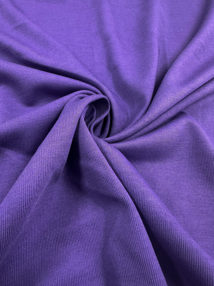 Close-up of Super Cheap Fabrics' 170cm Cotton Jersey in Patrician Purple, twisted and gathered at the center to create soft folds and shadows that enhance its rich texture and sheen.