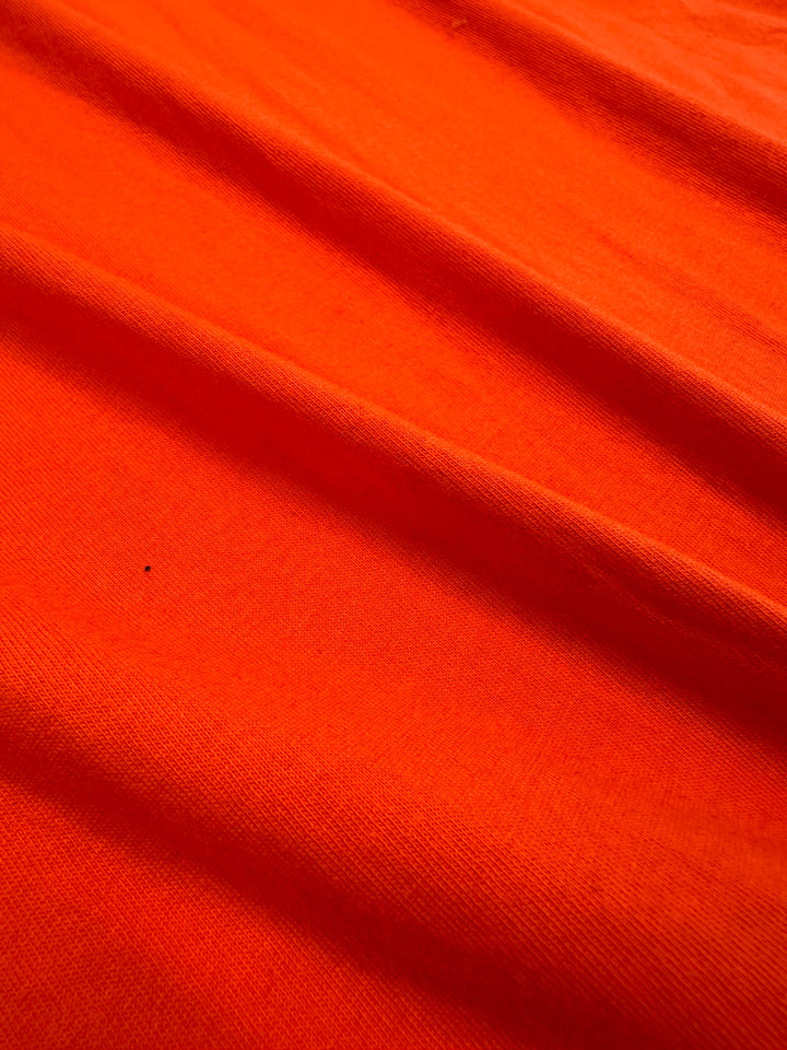 A close-up of tangerine-textured cotton jersey fabric, 155cm wide, from Super Cheap Fabrics showcases its soft and smooth texture with subtle creases. Ideal for light to medium weight garments, it’s reminiscent of Tangerine Tango's vibrant hue.