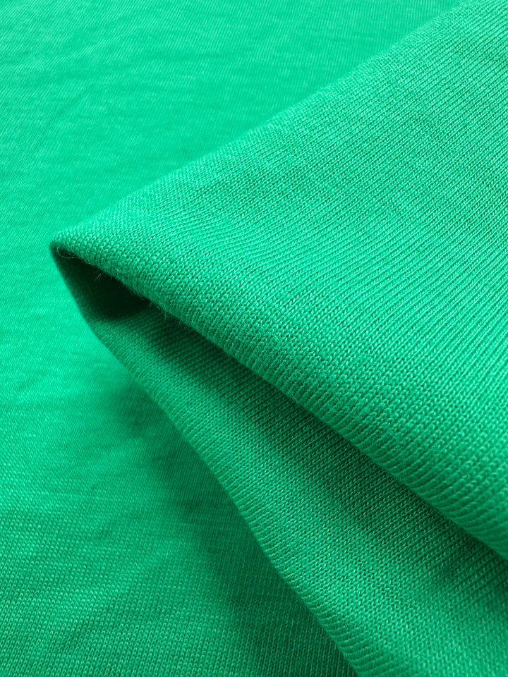 A close-up of Super Cheap Fabrics' Cotton Jersey in Vivid Green, 165cm, showcases its smooth textured surface. The neatly folded material highlights fine stitching, uniform coloration, and exceptional softness.