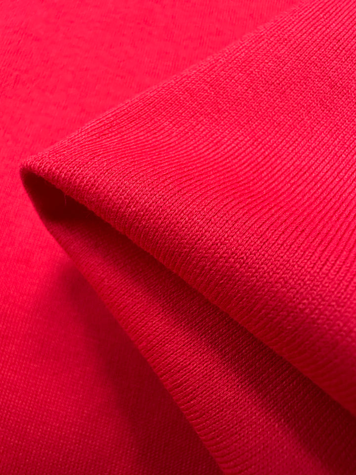 Close-up of folded Super Cheap Fabrics' Cotton Jersey - Ribbon Red, 165cm. The fabric is medium weight, soft, slightly ribbed with visible texture, and vibrant red color consistent across its surface.