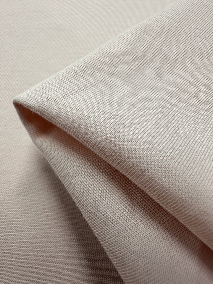 Close-up of Super Cheap Fabrics' Cotton Jersey in Rosewater, 165cm wide, neatly folded with a ribbed texture. Draped to highlight its smooth and soft appearance, this versatile fabric is ideal for crafting elegant clothing pieces.