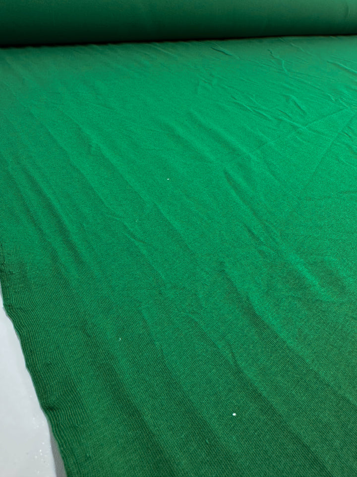 A close-up view of Super Cheap Fabrics' Cotton Jersey in Abundant Green, width 165cm, showcases its texture and subtle wrinkles.