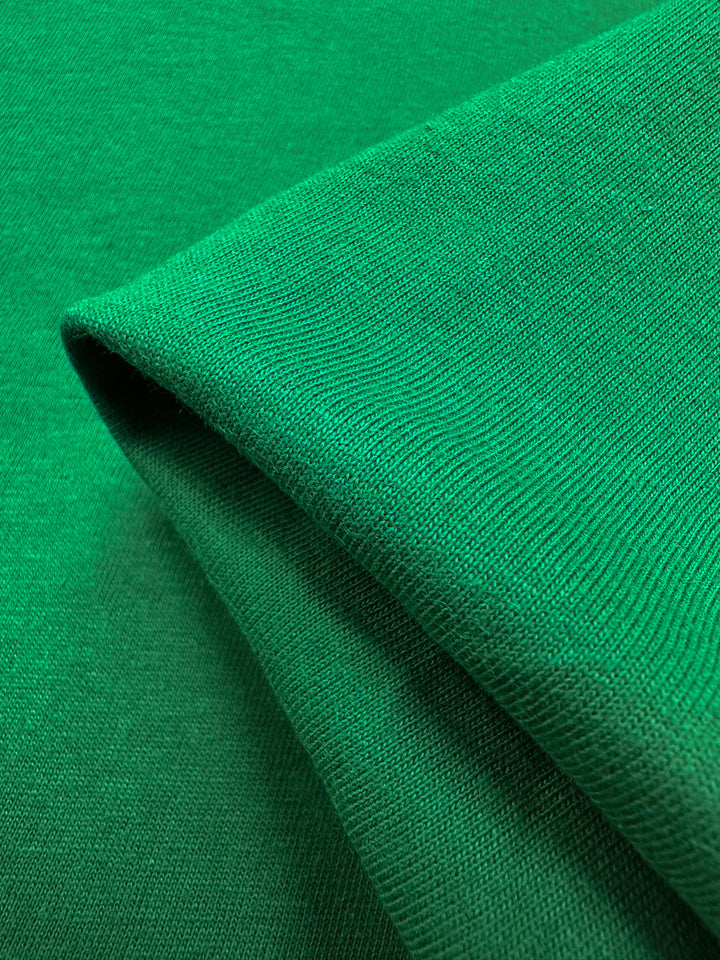 Close-up of Super Cheap Fabrics' Cotton Jersey in Abundant Green (165cm), showing its textured weave, neatly folded edge, and lightweight softness under lighting, giving a minimalistic appearance.