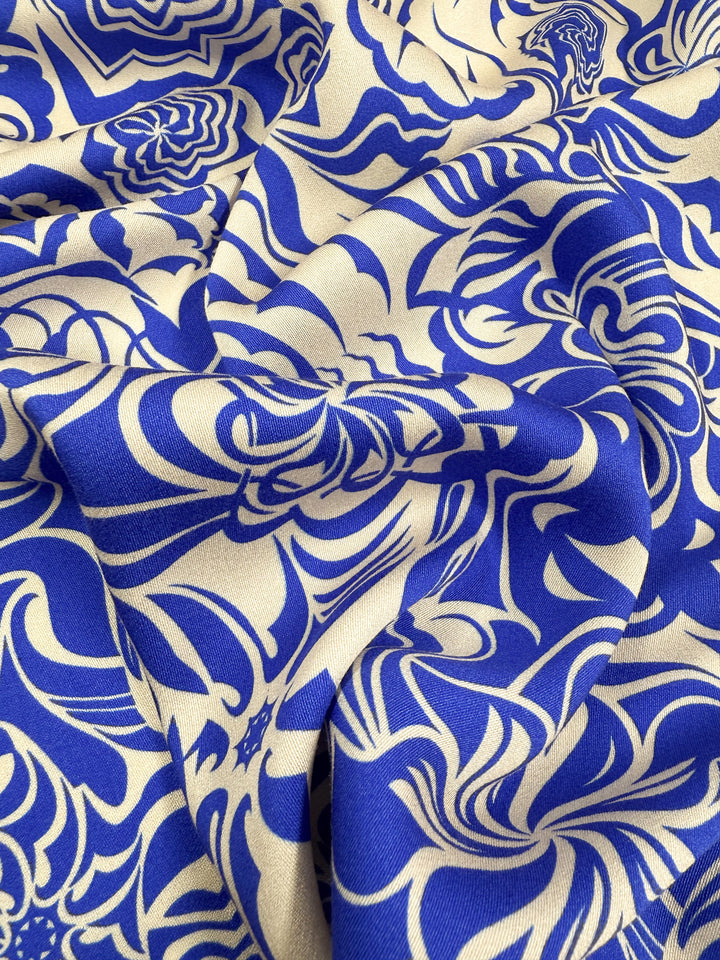 A close-up of Super Cheap Fabrics' Mercerised Rayon - Cobalt Whirl (150cm), showcasing breathable fabric with a blue and beige abstract floral pattern, flowing organic lines, and soft folds for added depth and texture.