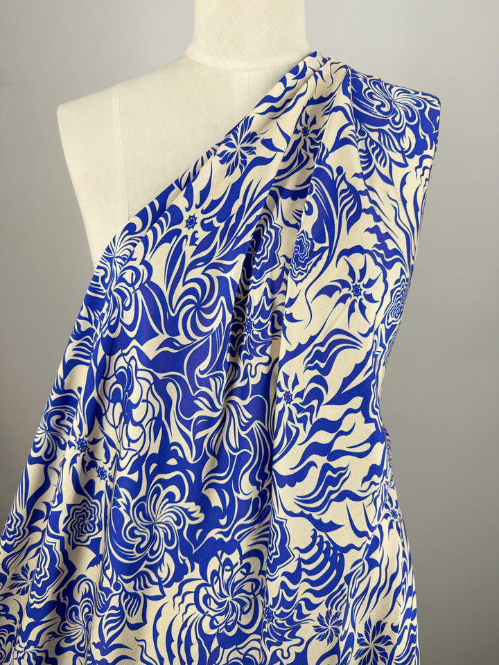 A mannequin showcases Super Cheap Fabrics’ Mercerised Rayon - Cobalt Whirl (150cm), a lightweight fabric with bold blue and white floral and swirl patterns, set against a light gray background.