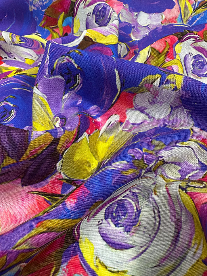 A close-up of Designer Rayon - Zoe - 145cm by Super Cheap Fabrics highlights its vibrant floral pattern featuring vivid prints in purple, yellow, pink, and white flowers for a bold look. Ideal for versatile creations!.