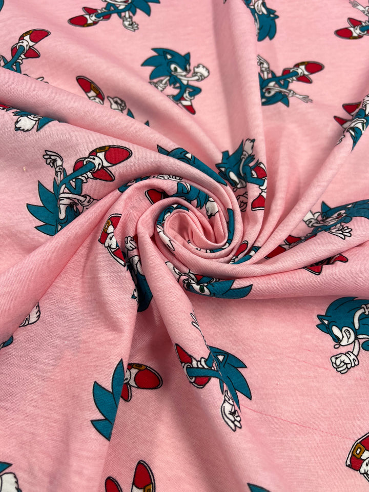 A detailed look at the "Printed Jersey - Sonic - 165cm" by Super Cheap Fabrics showcases a whimsical design featuring cartoon characters adorned with blue spikes, red shoes, and white gloves. The spiral twist in the Lycra material highlights various dynamic poses.