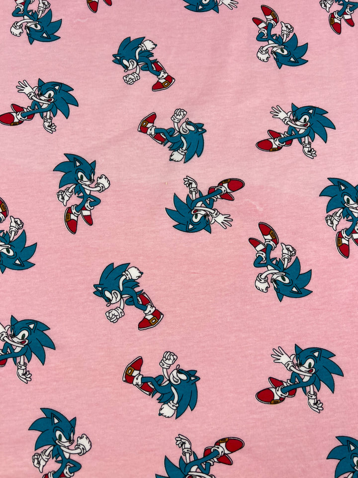 Explore the playful charm of our Printed Jersey - Sonic by Super Cheap Fabrics, showcasing delightful illustrations of an animated blue hedgehog striking various poses against a vibrant pink background. With red shoes and white gloves, this lightweight poly/cotton jersey fabric is perfect for adding a whimsical touch to any project.