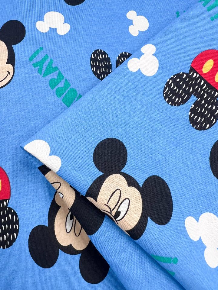 This medium-weight Printed Jersey from Super Cheap Fabrics, named "Mickey," features lively cartoon mouse patterns with black ears, smiling faces, and red shorts adorned with yellow buttons. White clouds and the whimsical word "HURRAY!" brighten this 170cm two-way stretch fabric.