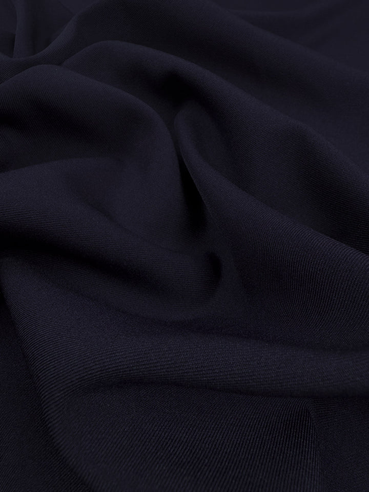 A close-up of Super Cheap Fabrics’ Liquid Twill - Black Iris (150cm) shows dark navy fabric with soft folds and a smooth, subtly textured surface, highlighting the refined quality of polyester.