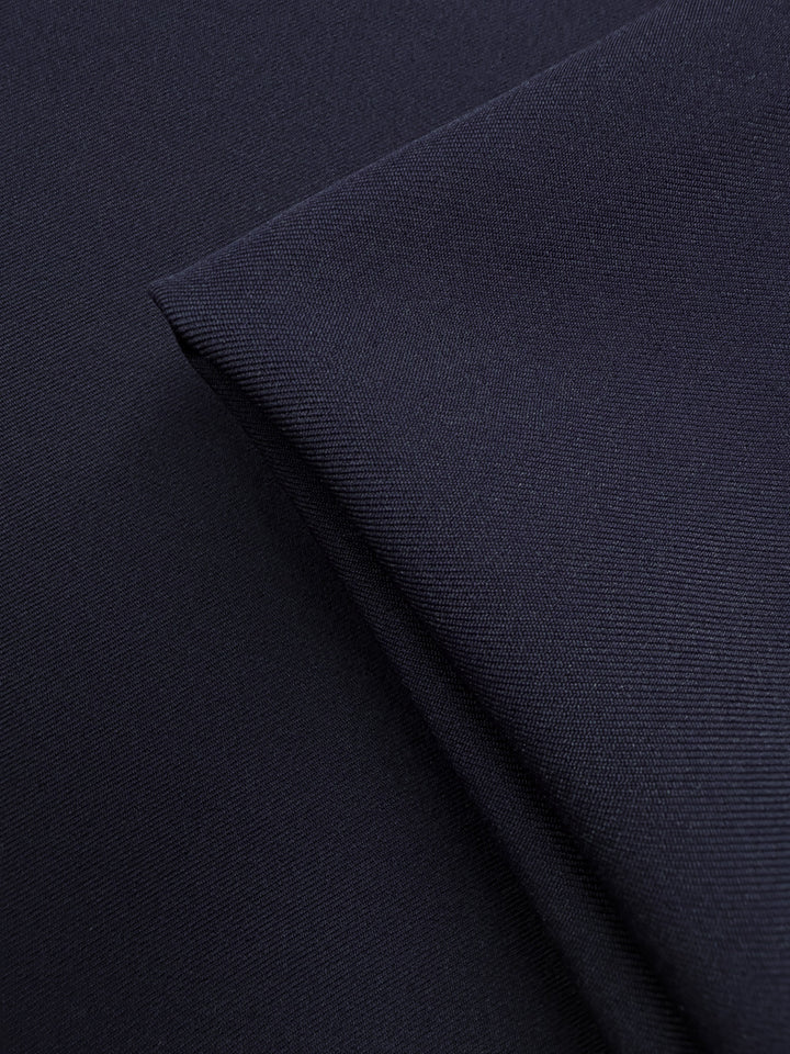 A close-up of Super Cheap Fabrics' Liquid Twill - Black Iris (150cm) highlights its dark navy blue color and distinct diagonal weave, with one section folded neatly over another.